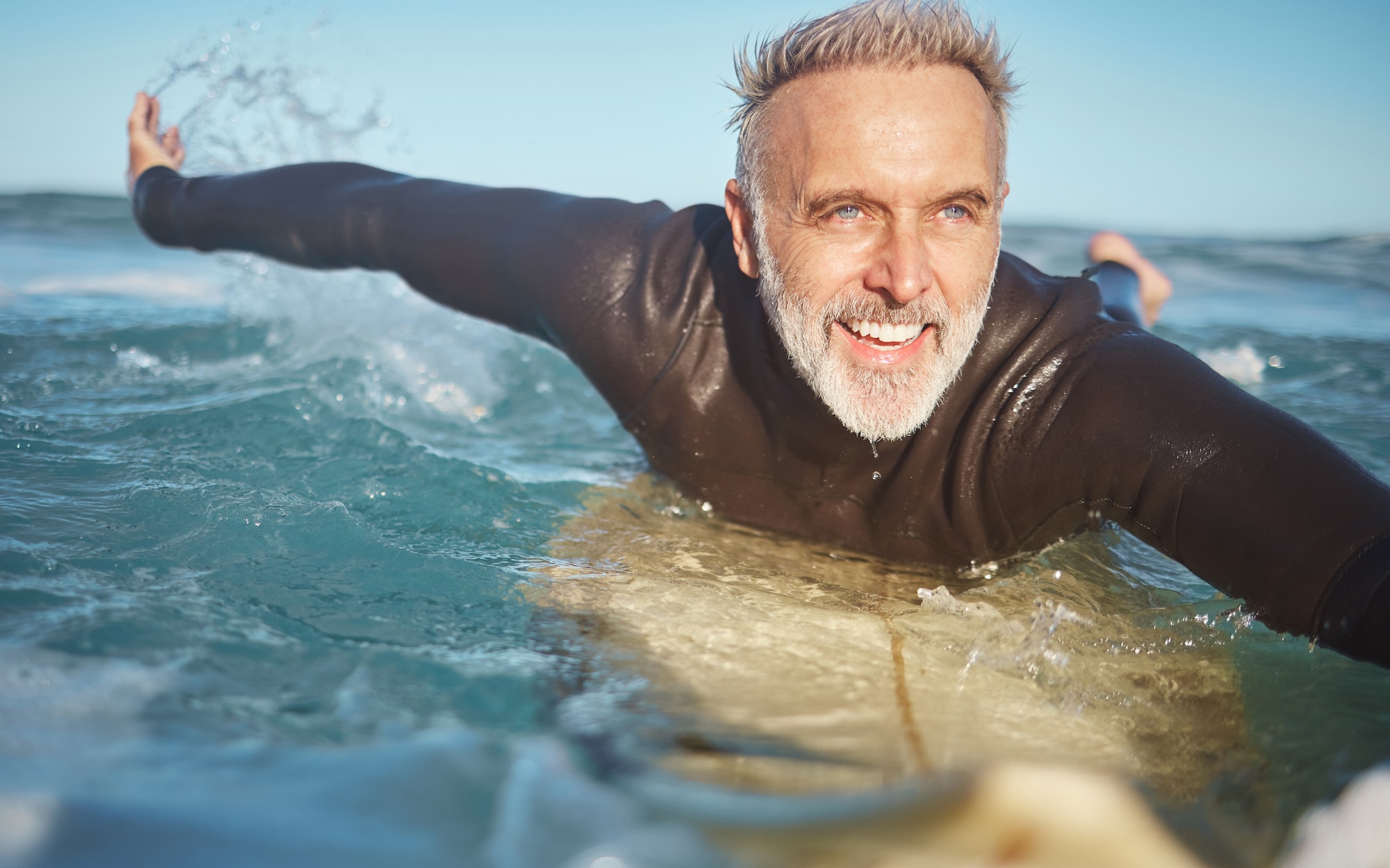 Beach, water and old man surfer swimming on a summer holiday vacation in retirement with freedom in
