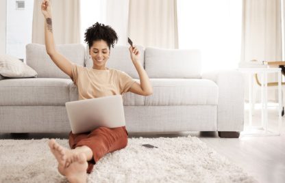 Black woman, laptop and happy with credit card, ecommerce and approved loan in lounge. Young female