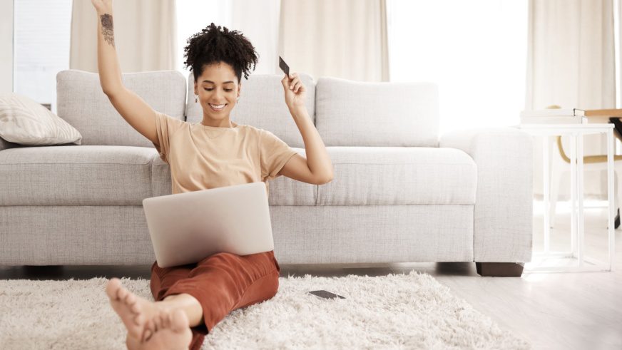 Black woman, laptop and happy with credit card, ecommerce and approved loan in lounge. Young female