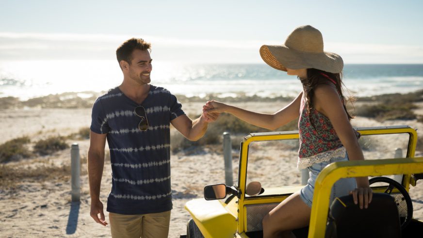 Happy caucasian couple on the beach assistance in getting out of the beach buggy