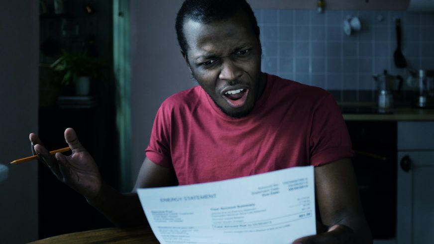Young frustrated african american man looks at bill, worried about troubles with payments